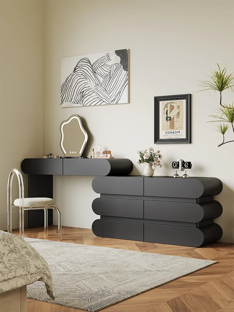 The bedroom is modern and simple, with a makeup table, cream style, black corner dresser and chest of drawers.