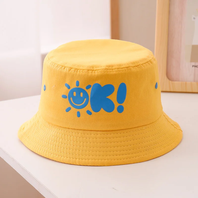 Eine modische und niedliche, zickzackförmige, sonnenfarbene Babymütze mit lächelndem Gesicht und OK-Bubble-Print, geeignet für den Sonnenschutz am Strand