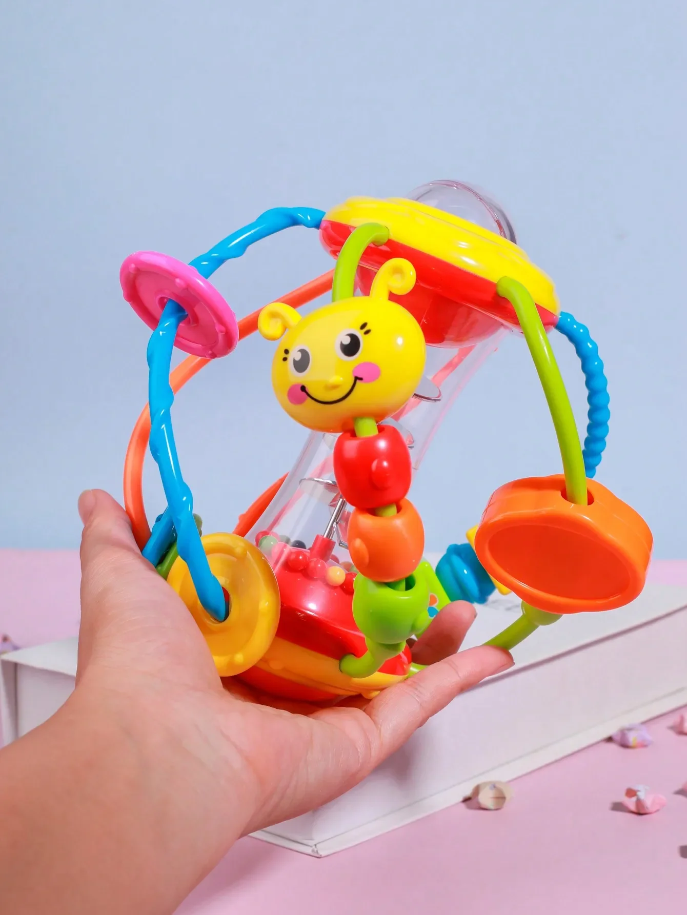 Randomly colored. A rattle activity ball toy designed for infants aged 12 months, featuring swaying arms and rotating rattles.