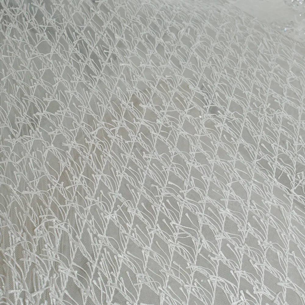 Weißer Spitzenstoff mit Fransen und der strukturierte, netzähnliche Stoff für Hochzeitskleider und formelle Kleider