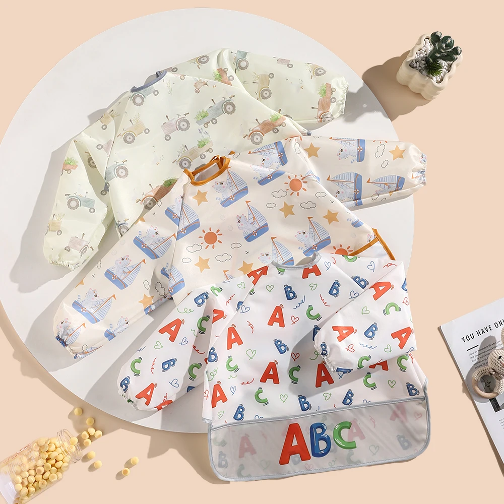 

A cartoon-patterned feeding bib with long sleeves and a pocket, featuring tie straps, suitable for children aged 2-6