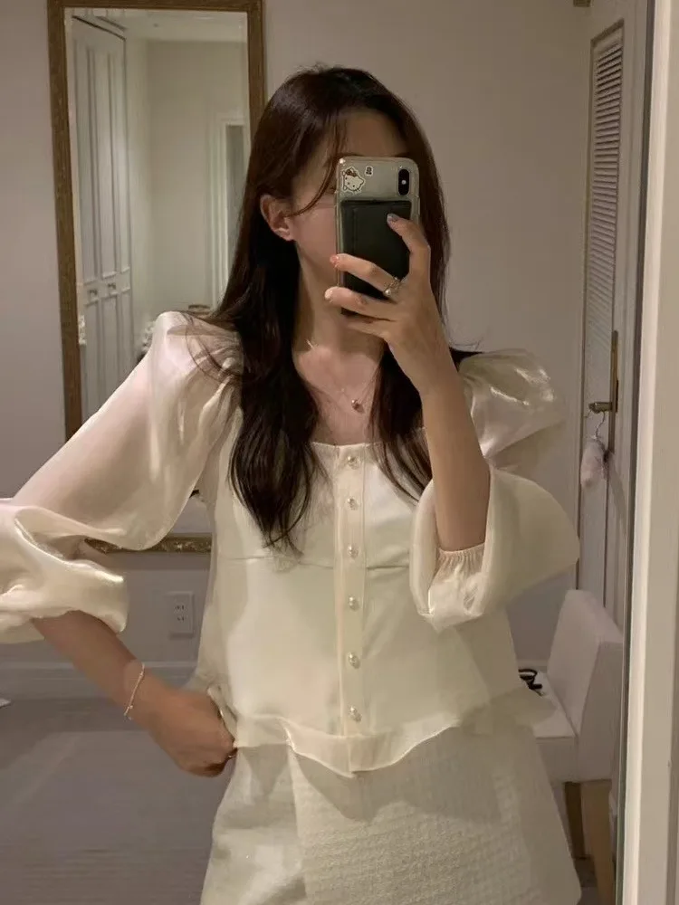 قميص أنيق بياقة مربعة وأكمام منتفخة مع أزرار دقيقة وحواف دانتيل، يضفي أجواء نهاية العام، مزين باللؤلؤ واللمعان وأكمام طويلة