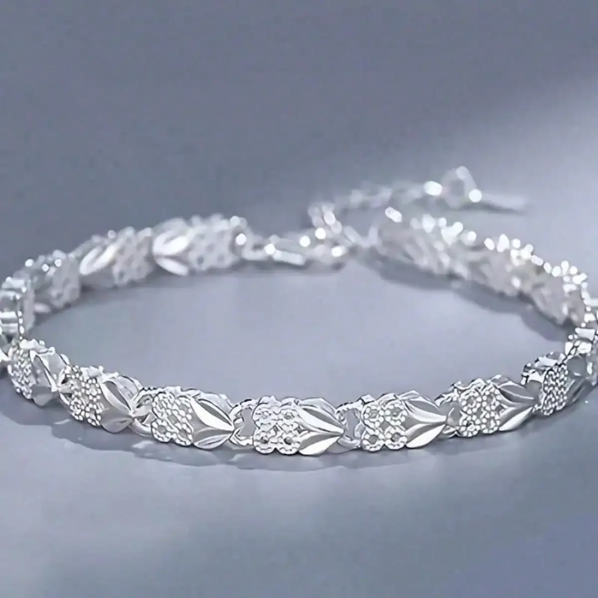 Una hermosa pulsera plateada adornada con hojas y flores, pulida hasta lograr un brillo deslumbrante. La cadena ajustable se adapta a varios tamaños de muñeca, perfecta para uso diario o fiestas. Como un regalo atemporal: elegante, duradero y con estilo.