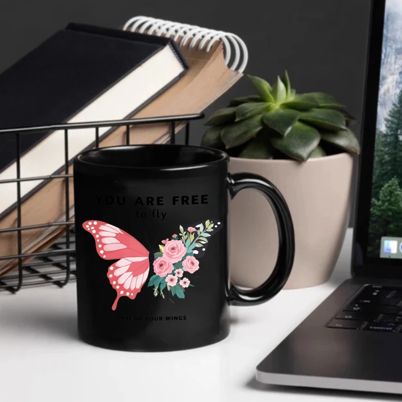 A black ceramic mug with a pink butterfly and floral design and an inspirational quote to 