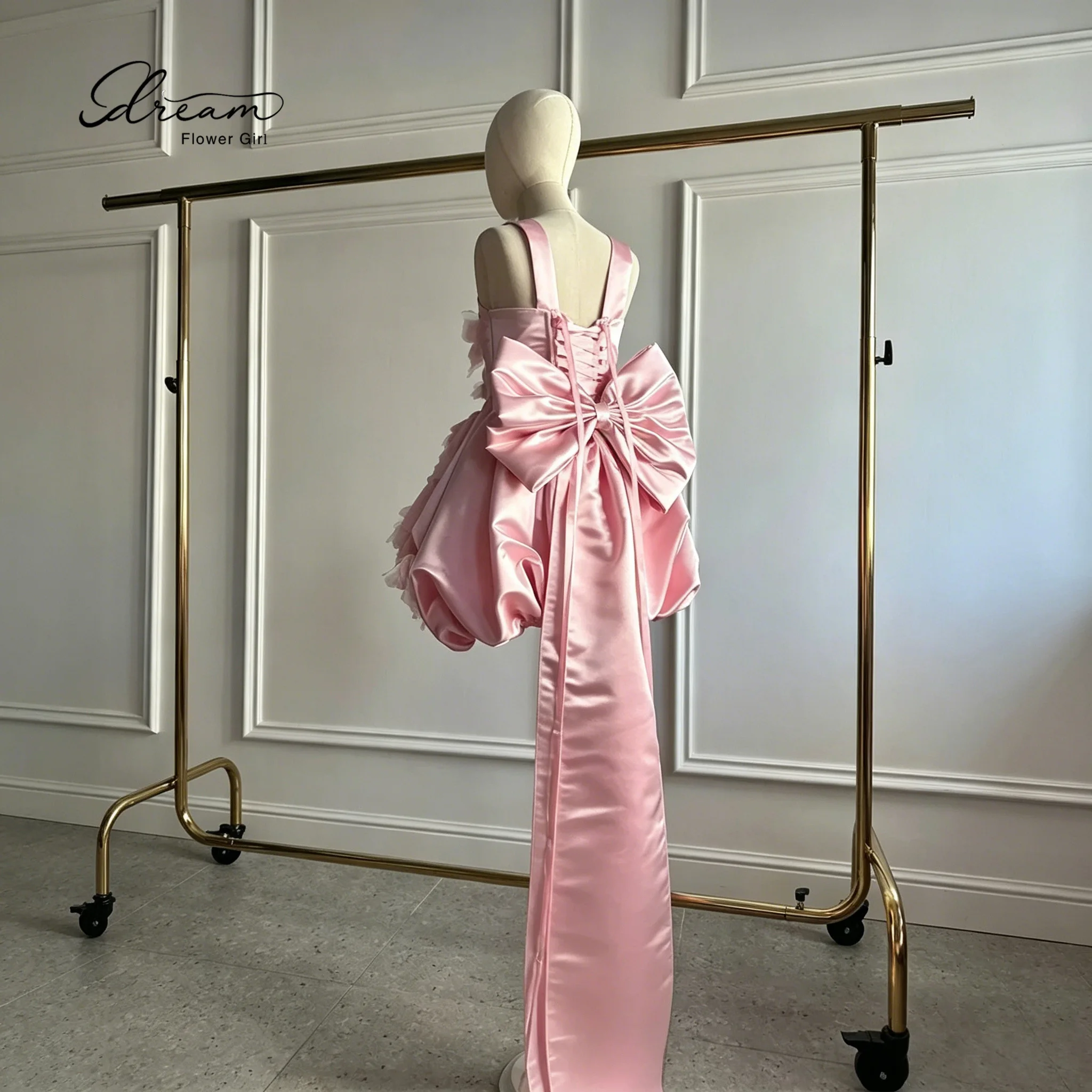 Adorable flower girl's pink satin knee-length evening dress, adorned with butterfly decorations and a bow design at the back.