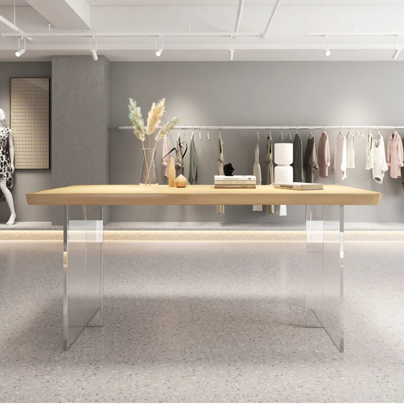 In the clothing store, the island display table,  and the simple rectangular shelves in acrylic are placed