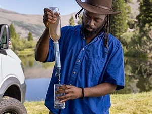 Man squeezing a bottle of dirty water through the filter to have clean water in drinking glass