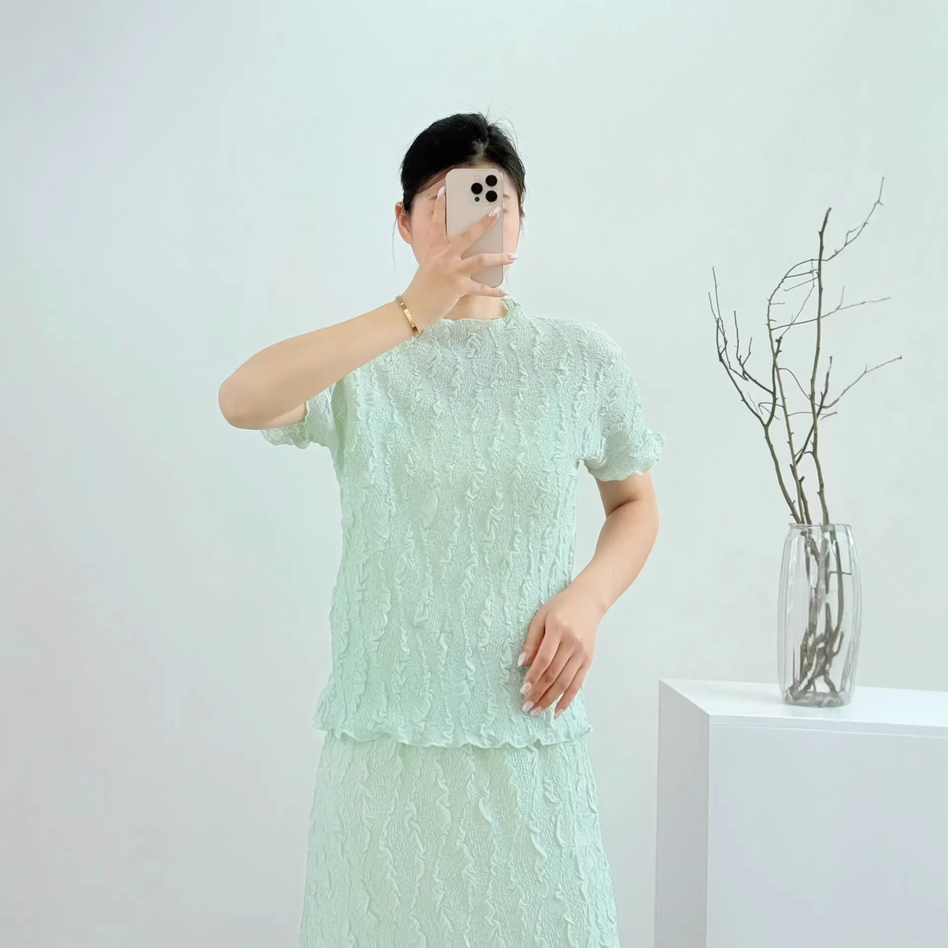 

Элегантный мятно-зеленый текстурированный плиссированный комплект из двух предметов от Miyake: топ с коротким рукавом, воротником-стойкой и рюшами, а также прямая юбка.