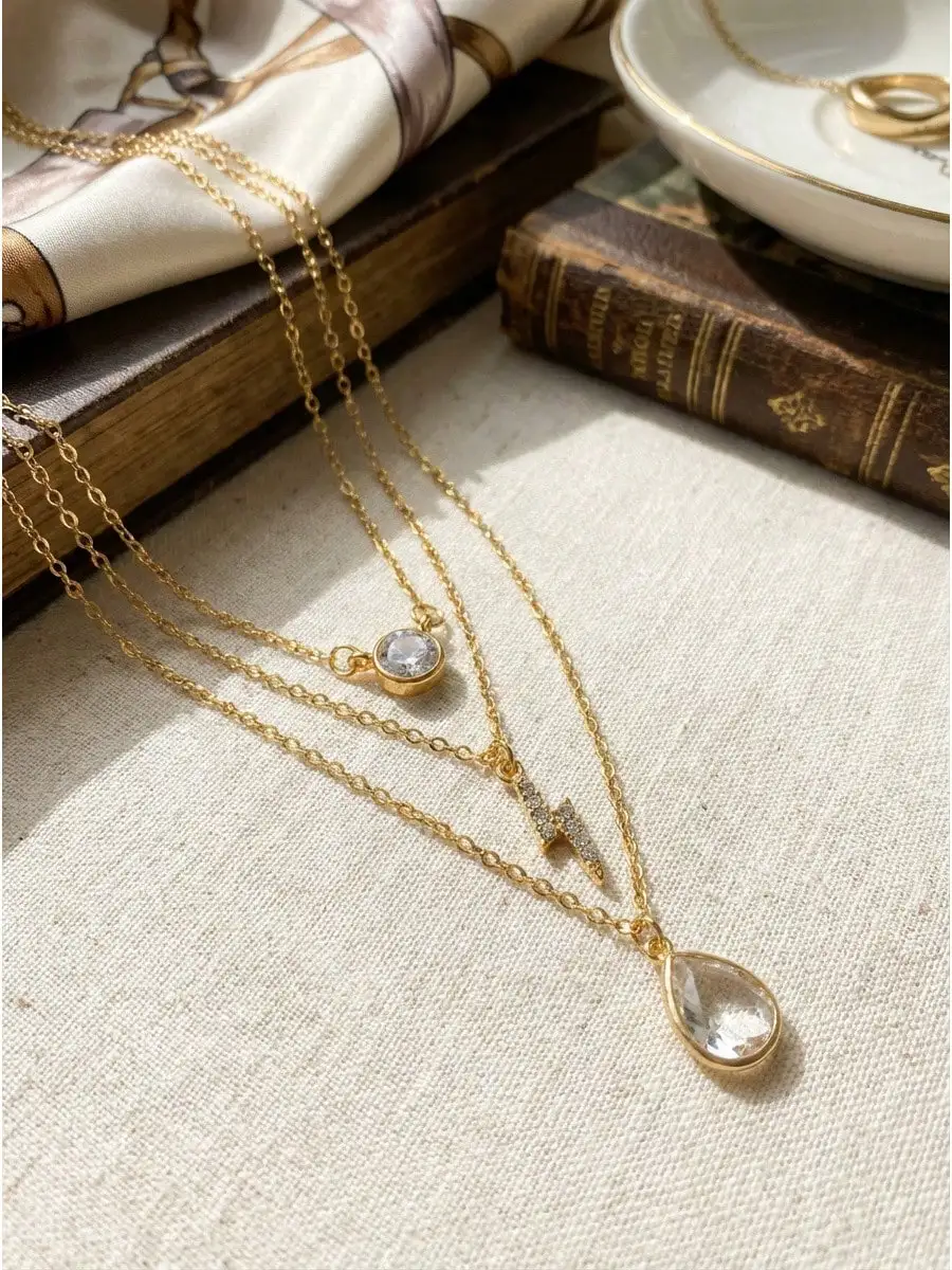 

Многослойное золотистое ожерелье с подвесками в виде кристаллического круга, молнии и капли.