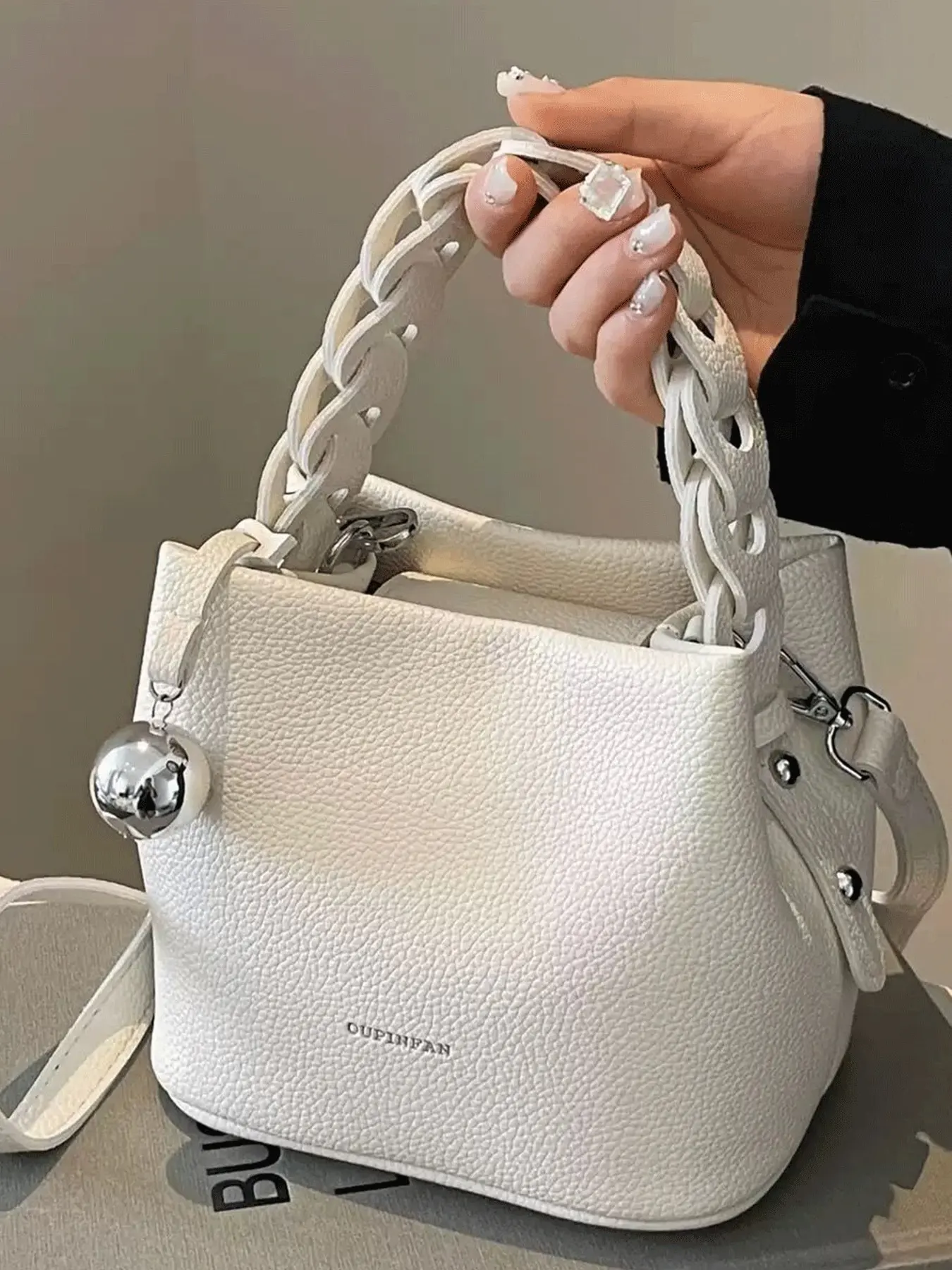 

Белая текстурированная сумка-ведро из искусственной кожи с верхней ручкой, плетеным ремешком и металлическим кулоном