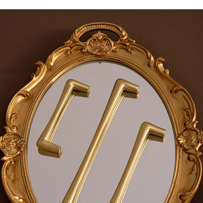 Three slim brass cupboard pulls reflected in a gold mirror