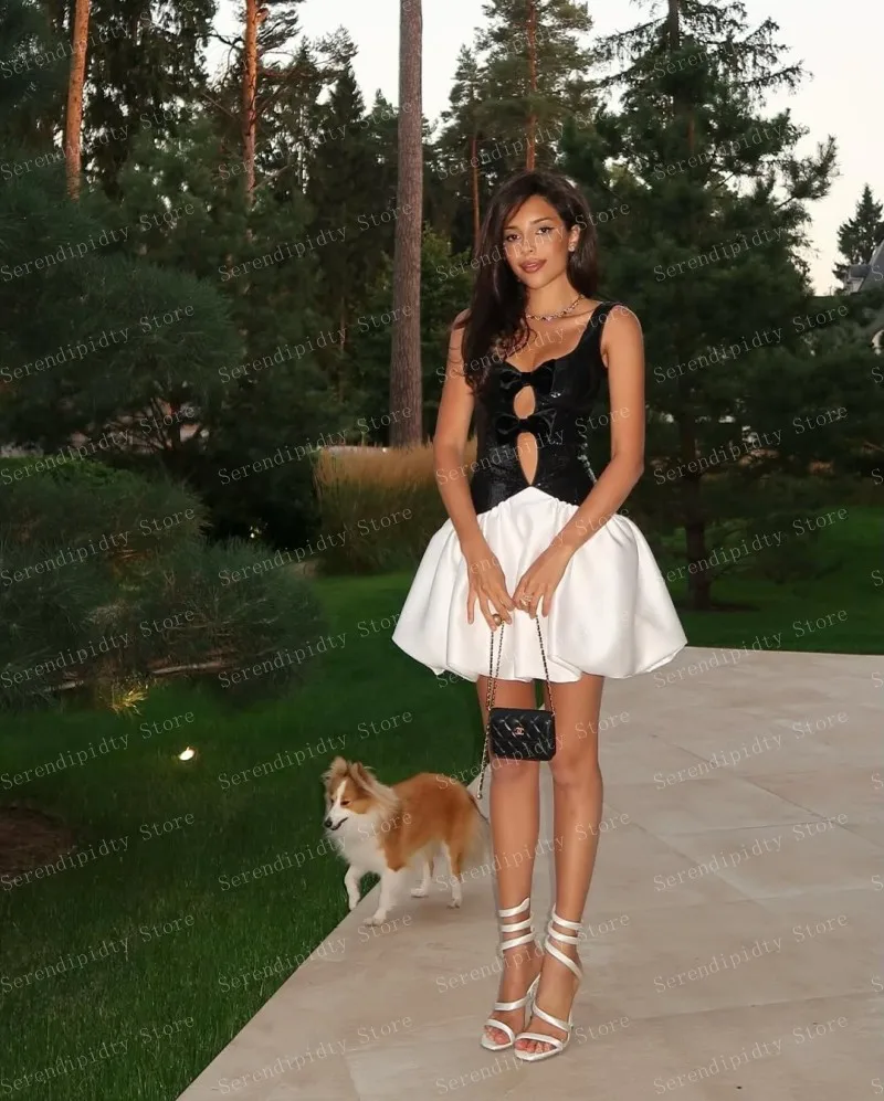 Haut à paillettes noir poli avec grand nœud et jupe en satin blanc, design ajusté révèle le ventre associé à un sac à sangle en chaîne