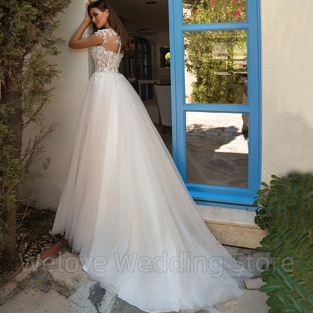 Nowoczesna suknia ślubna z tiulowymi aplikacjami, krótkimi rękawkami, iluzorycznym tyłem z guzikami, trenem typu sweep, długa do podłogi, formalna suknia ślubna.