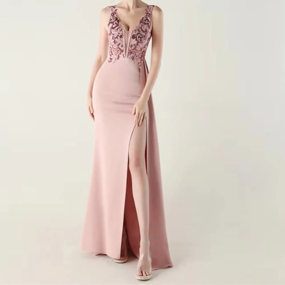 Vestido de noche de sirena sin mangas, color rosa palo, con escote en V pronunciado, aplicaciones de encaje, abertura lateral alta y cinturón flotante, ideal para fiestas formales.