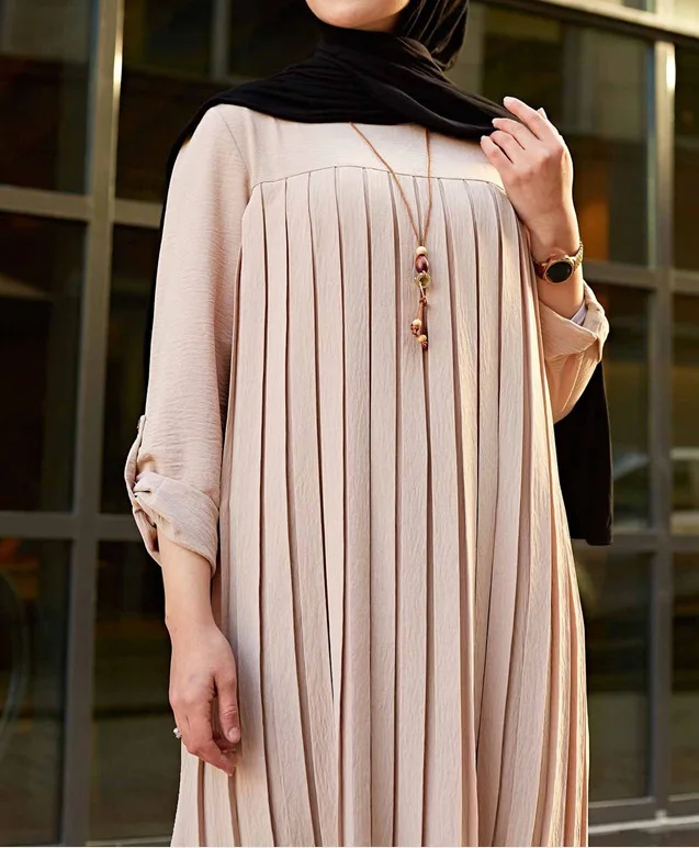 Close-up of beige pleated tunic showing the round neckline and rolled sleeves