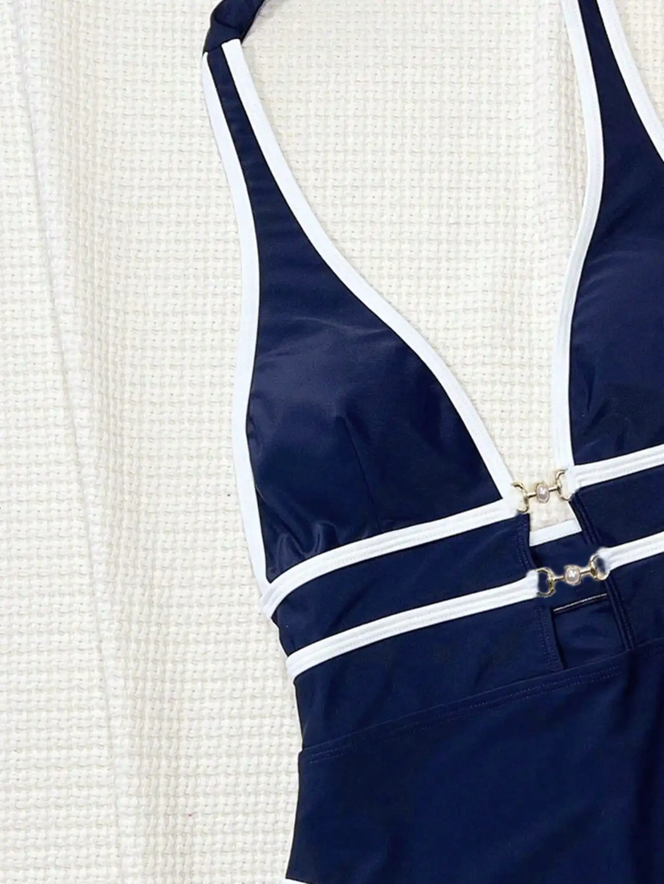 

Слитный купальник темно-синего цвета с глубоким V-образным вырезом, белой отделкой и жемчужными пряжками