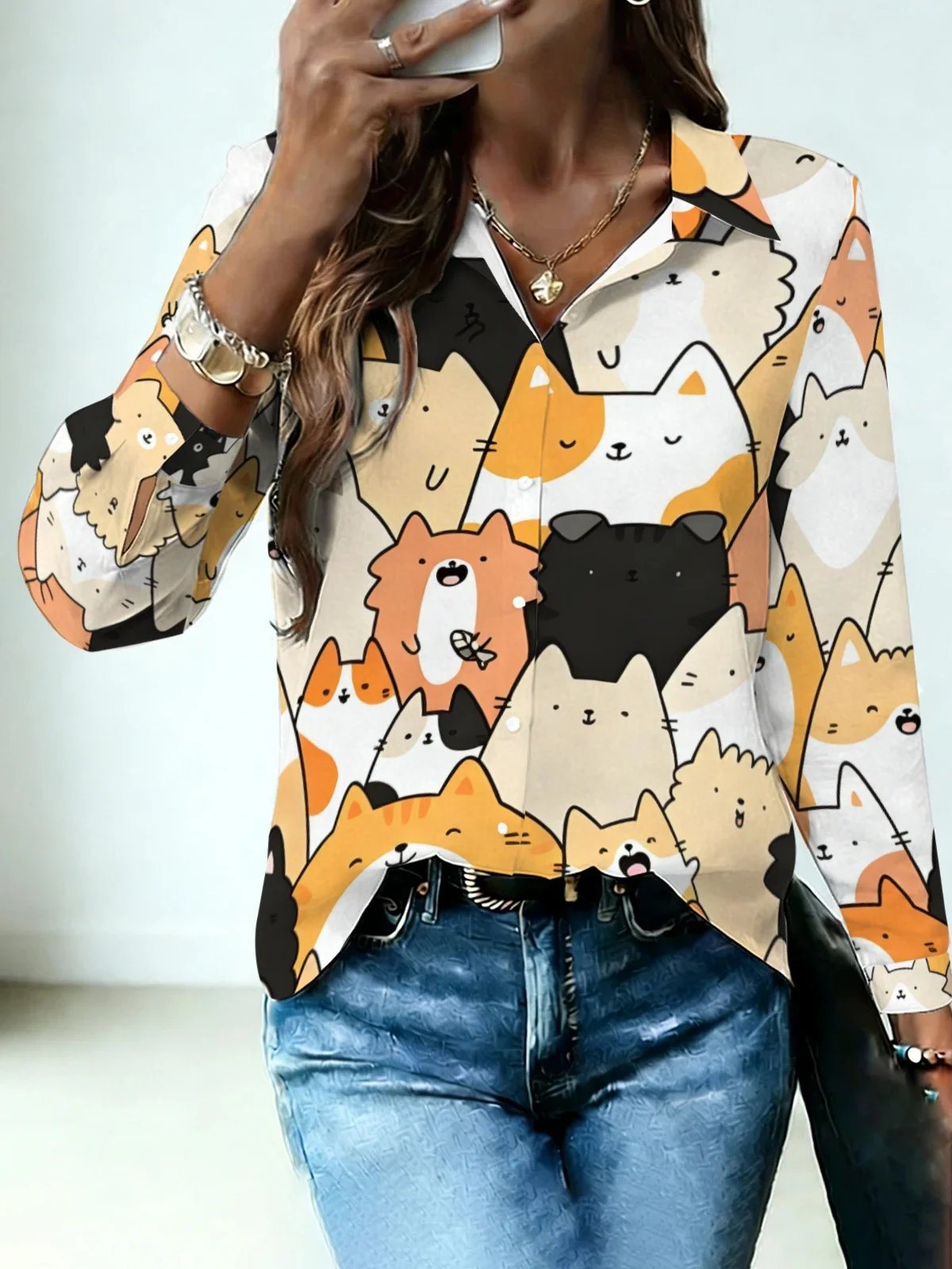 Camisa de mujer con cuello, minimalista, en tonos cálidos, con estampado integral de gatos de dibujos animados en naranja y negro sobre base blanco roto, de manga larga.