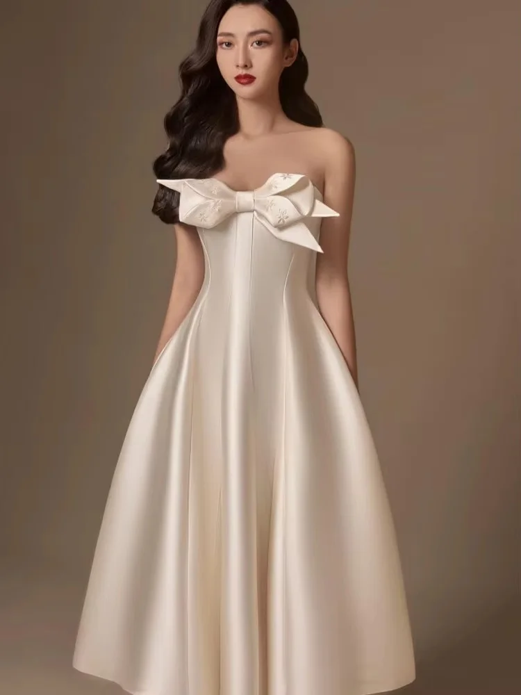 Strapless midi gown decorated with three-dimensional big bow. Loose flared skirt looks light and elegant, plain white brings cla