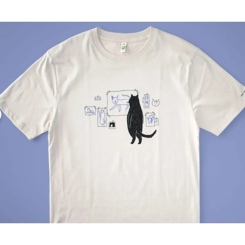 تي شيرت Cat Gallery مطبوع يدويًا على تي شيرت من القطن العضوي باللون البيج مع رسم توضيحي باللونين الأسود والأزرق لفن القطط القاضي