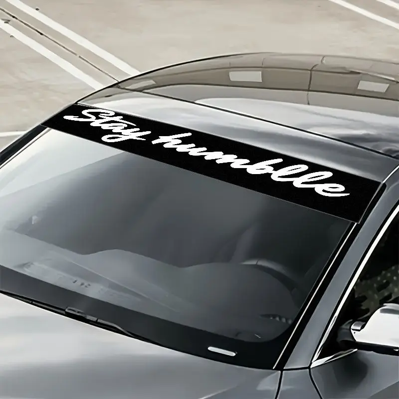 

A stylish handwritten sticker with the words "Stay Humble" on the front windshield of a car, featuring stylish white letters and