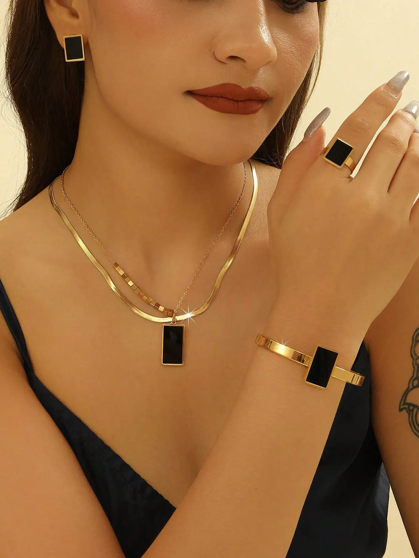 

Набор украшений для женщин: колье с прямоугольным кулоном золотистого цвета, серьги, браслет и кольцо.