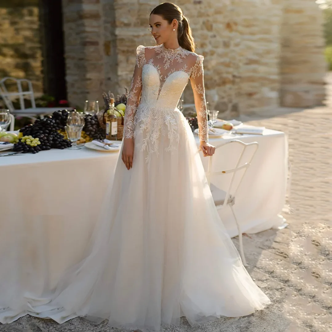 Elegancka suknia ślubna szyta na miarę, z wysokim dekoltem, długimi rękawami, iluzoryczną koronką, aplikacjami, tiulową spódnicą w kształcie litery A, trenem zamiatającym.