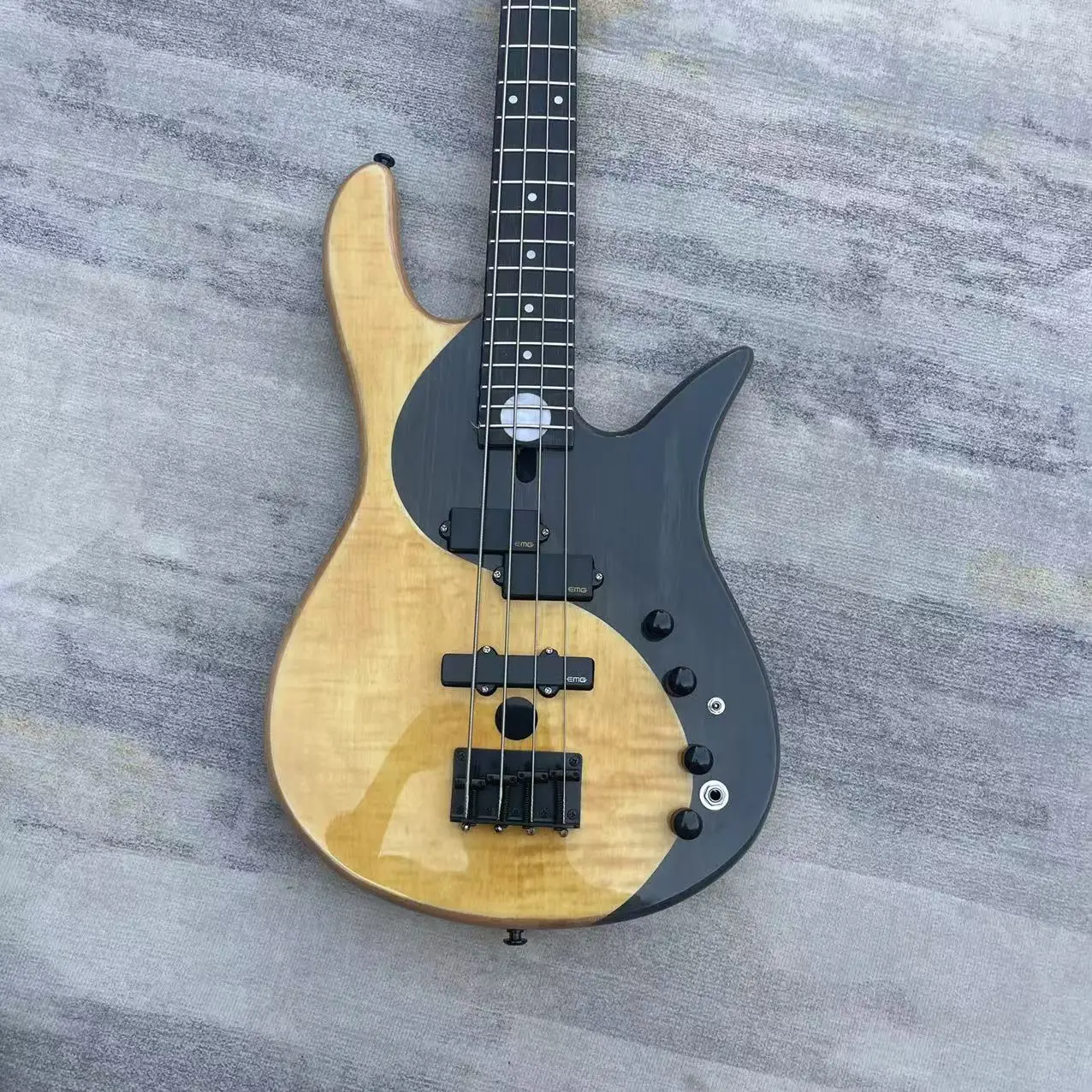 Electric bass 4 chord yin-yang butterfly style electric bass, with a natural wood color body and black accessories. Factory phot