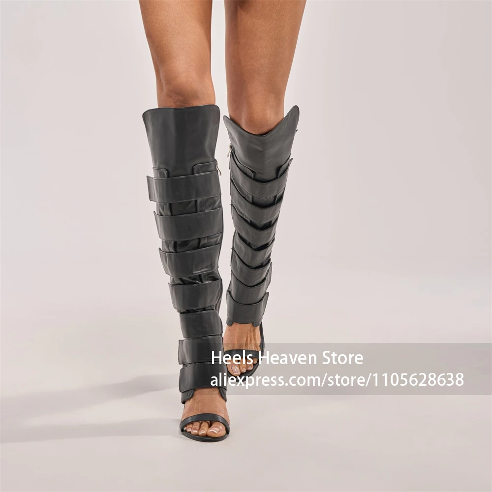 Botas gladiador de tacón de aguja negras, con diseño de correa ancha en capas, talón sobre la rodilla, caña recortada, de piel sintética lisa negra y estilo atrevido.