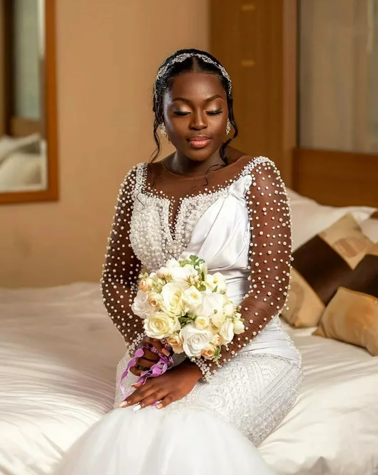 ชุดแต่งงานแบบแอฟริกันสั่งตัดพิเศษ คอเสื้อโปร่งประดับมุกเงางาม พร้อมชายกระโปรงยาวแบบสปีว์เทรน แขนยาวคลาสสิก หรูหรา