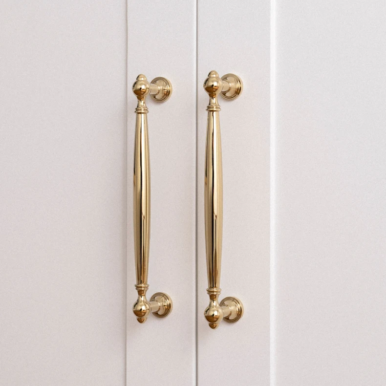 Pair of gold drawer pulls mounted vertically on white doors
