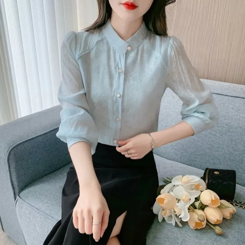 

Женская блузка светло-голубого цвета с элегантным воротником-стойкой, рукавом 3/4 и жаккардовым узором, полупрозрачная.