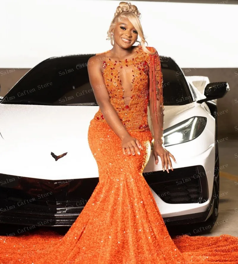 فستان برتقالي مزين بالترتر مع ذيل طويل وفتحة رقبة على شكل V عميقة يلمعًا على الطراز يقف بجانب ثوب الزفاف الفاخر