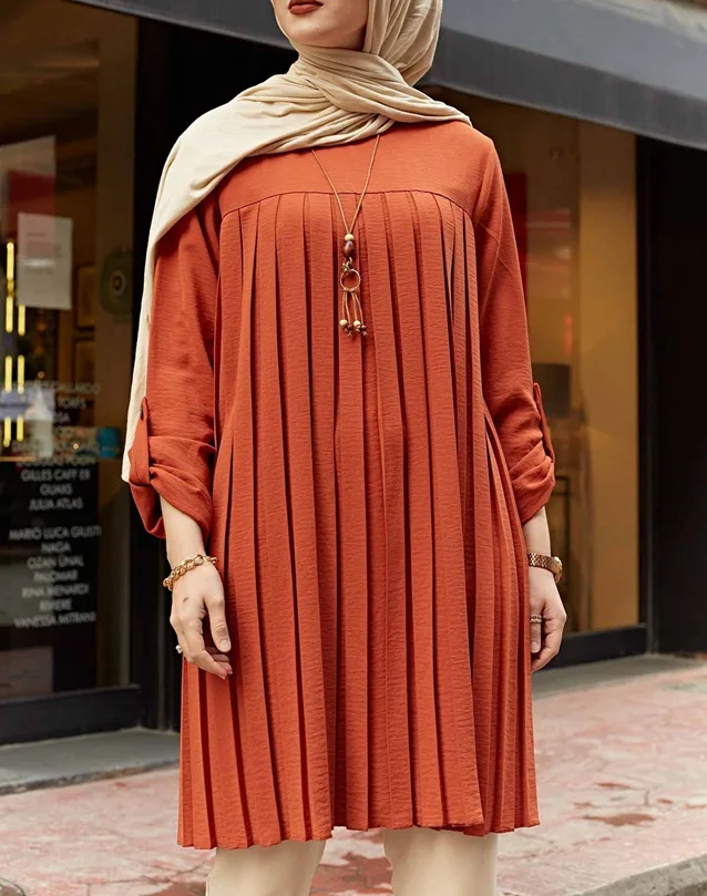 Front view of rust pleated tunic with round neckline and rolled sleeves