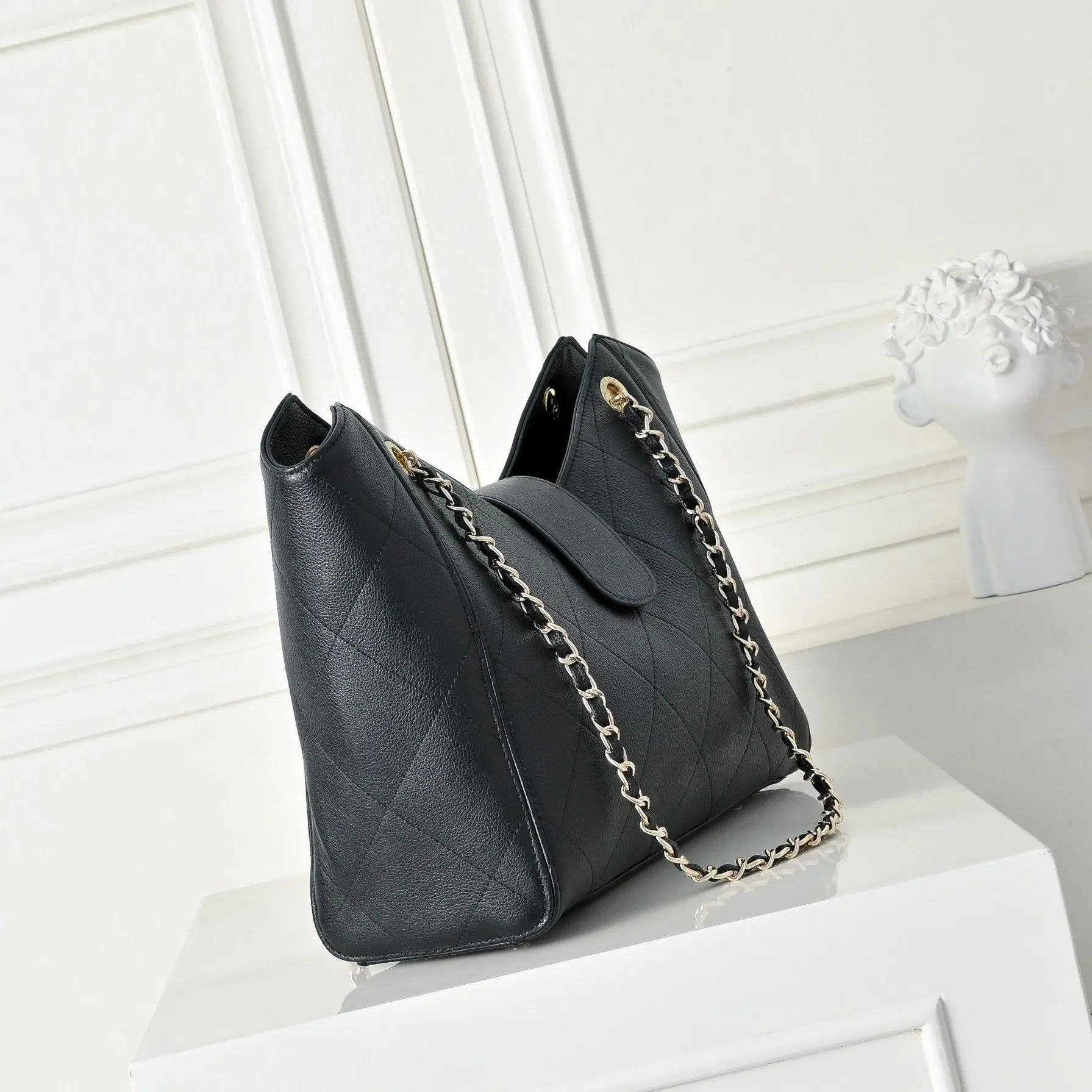 

Black quilted leather tote bag with interwoven chain straps, magnetic flap closure and matching pouch.