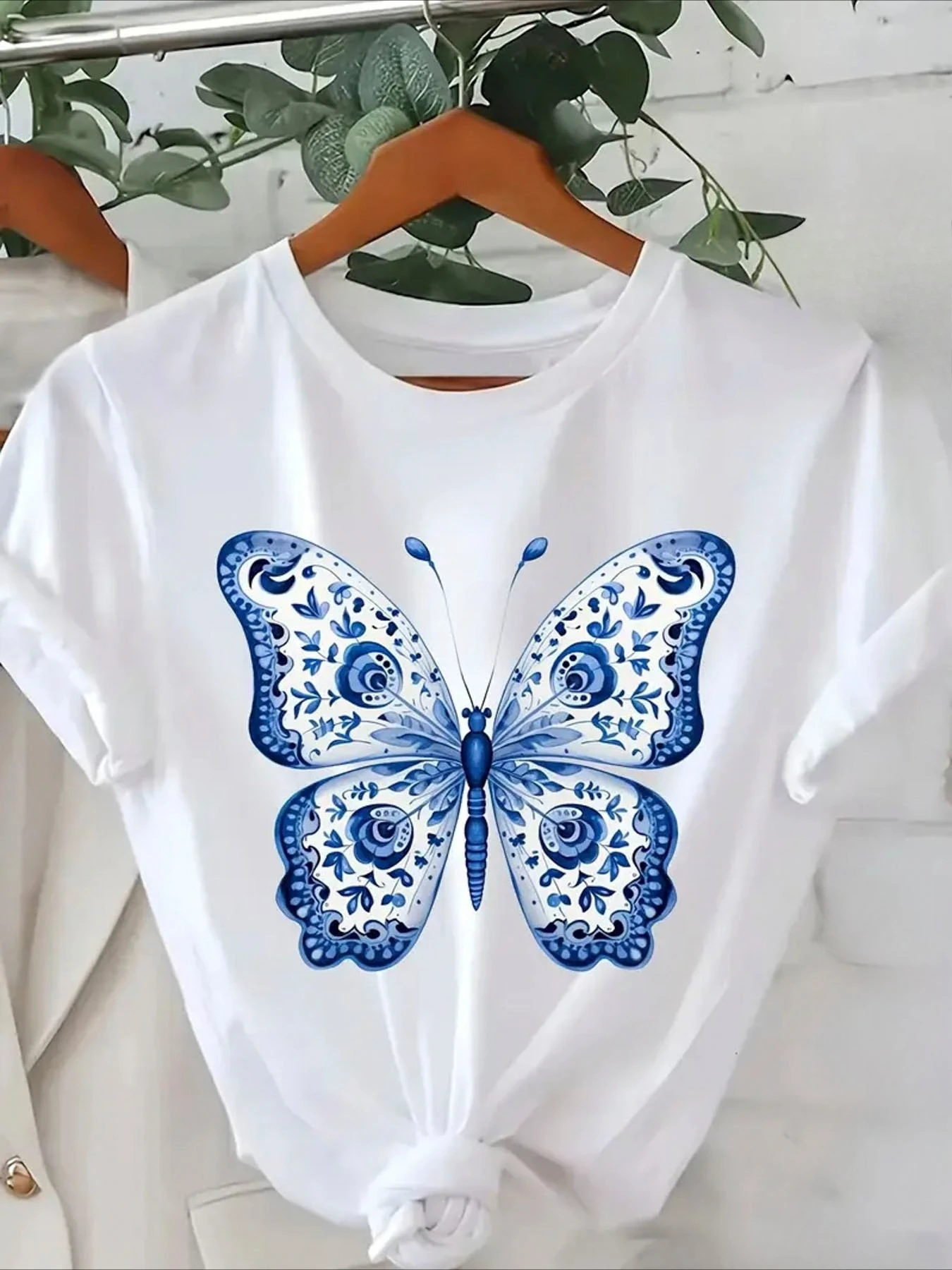 Showcasing A Blue and Butterfly Motif with Intricate Hung Against Background of Green Foliage White Aesthetic Clothes