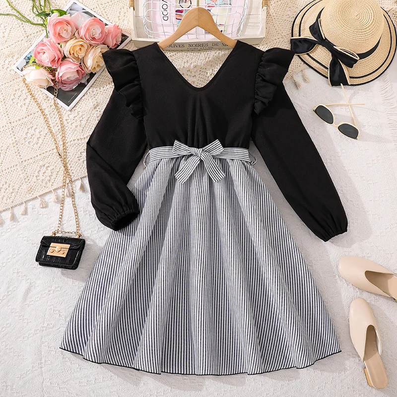 

Повседневное черно-белое контрастное платье для девочек 8-12 лет: с V-образным вырезом, рюшами на плечах, полосатой юбкой и завязывающимся бантом на талии.