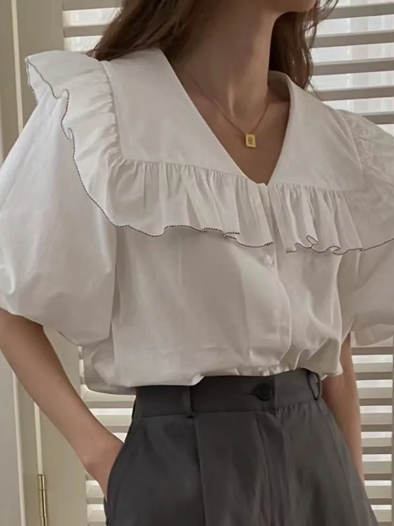 Csa fena e e simples com gola azul marinho, manga bufante com babados e botão único, estilo verão.