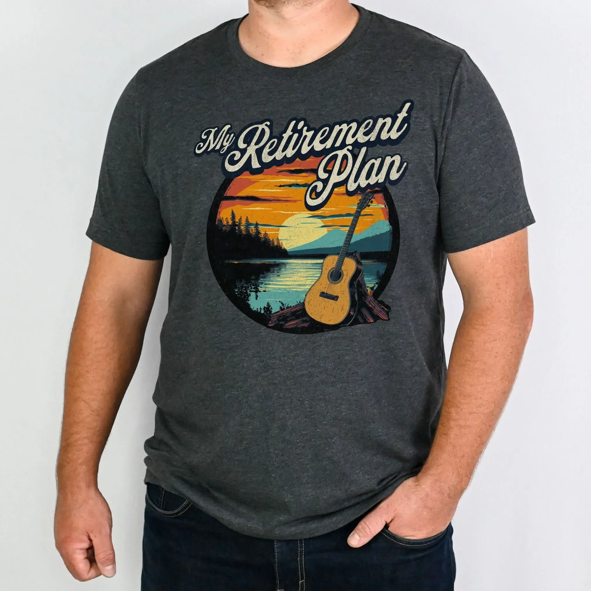 Camiseta 'My Retirement Plan' com estampa de guitarra acústica, cenário natural ao pôr do sol, músico relaxado