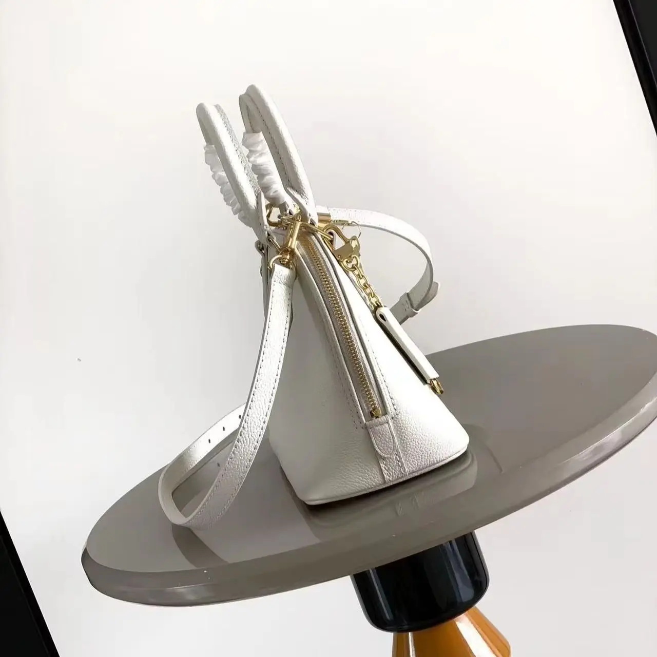 White pebble-grain leather mini dome bag with gold lock and key hardware, top handle, and detachable slim crossbody strap.