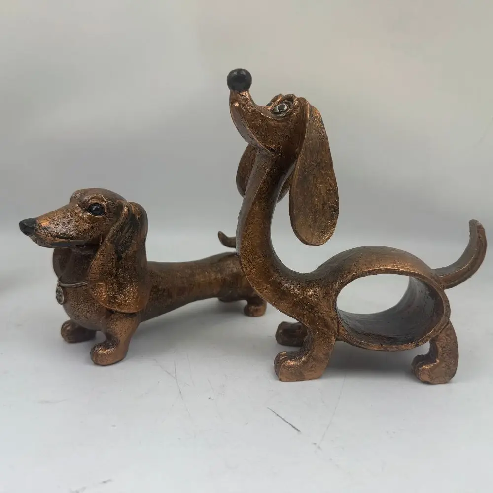 A collection of rustic style resin dachshund figurines in beige and dark bronze colors, displaying both classic long sausage dog poses and a stylized upward-stretching posture on bookshelves and desks.