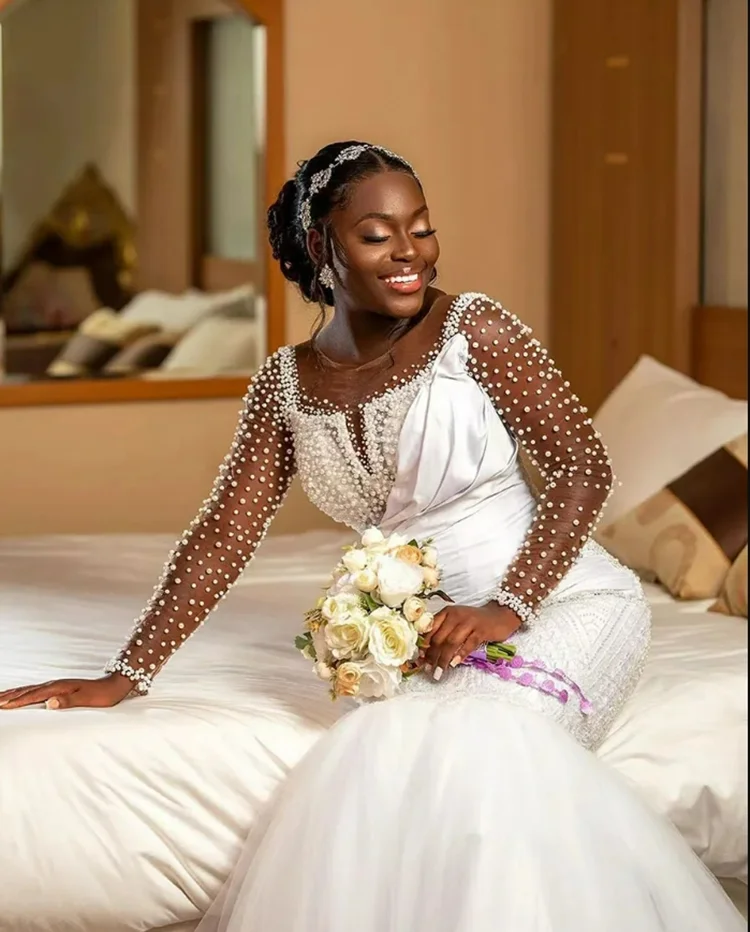 ชุดแต่งงานแบบแอฟริกันสั่งตัดพิเศษ คอเสื้อโปร่งประดับมุกเงางาม พร้อมชายกระโปรงยาวแบบสปีว์เทรน แขนยาวคลาสสิก หรูหรา