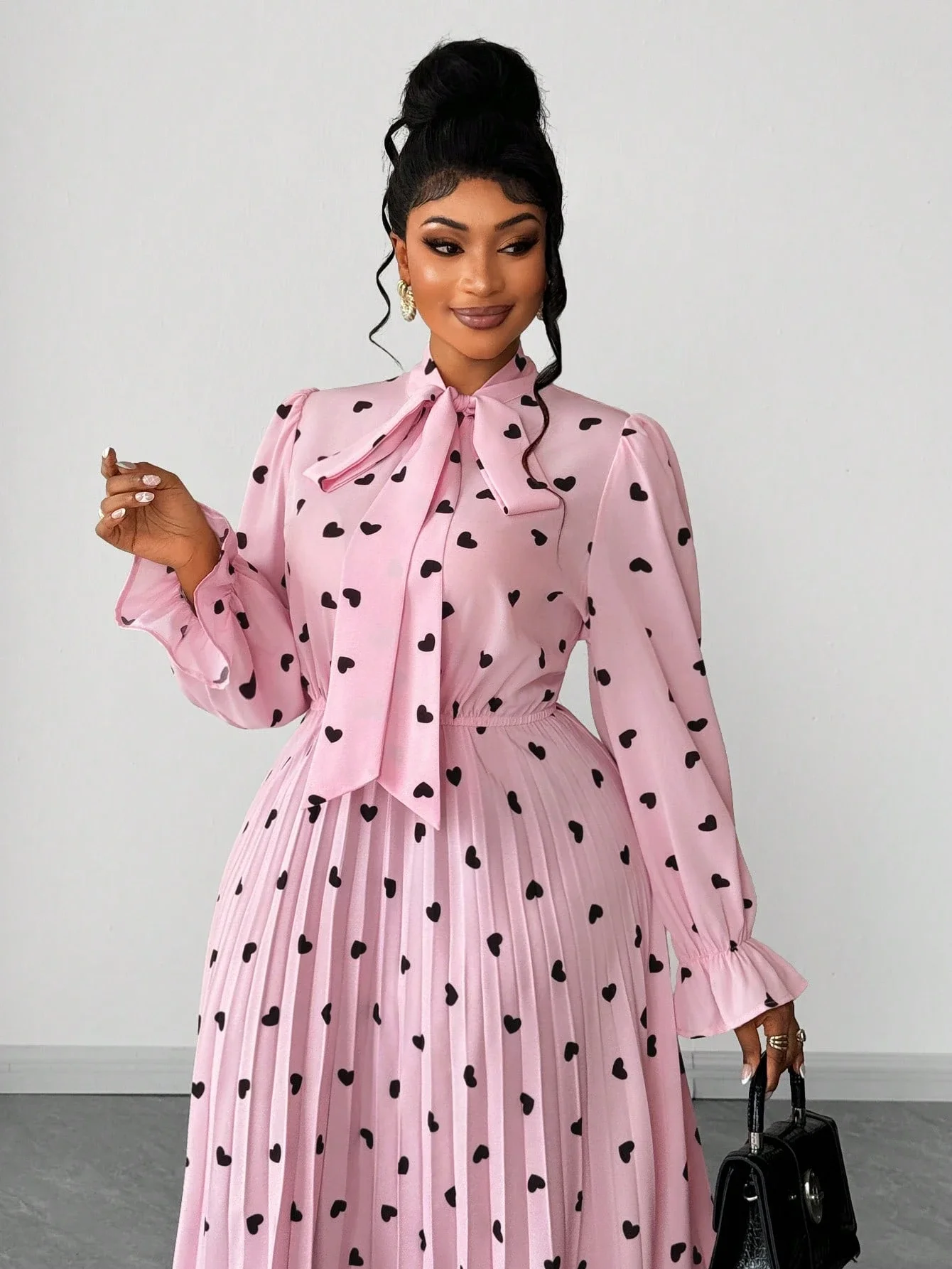 

Розовое плиссированное макси-платье с принтом в виде сердечек, бантом на горловине и рукавами с рюшами