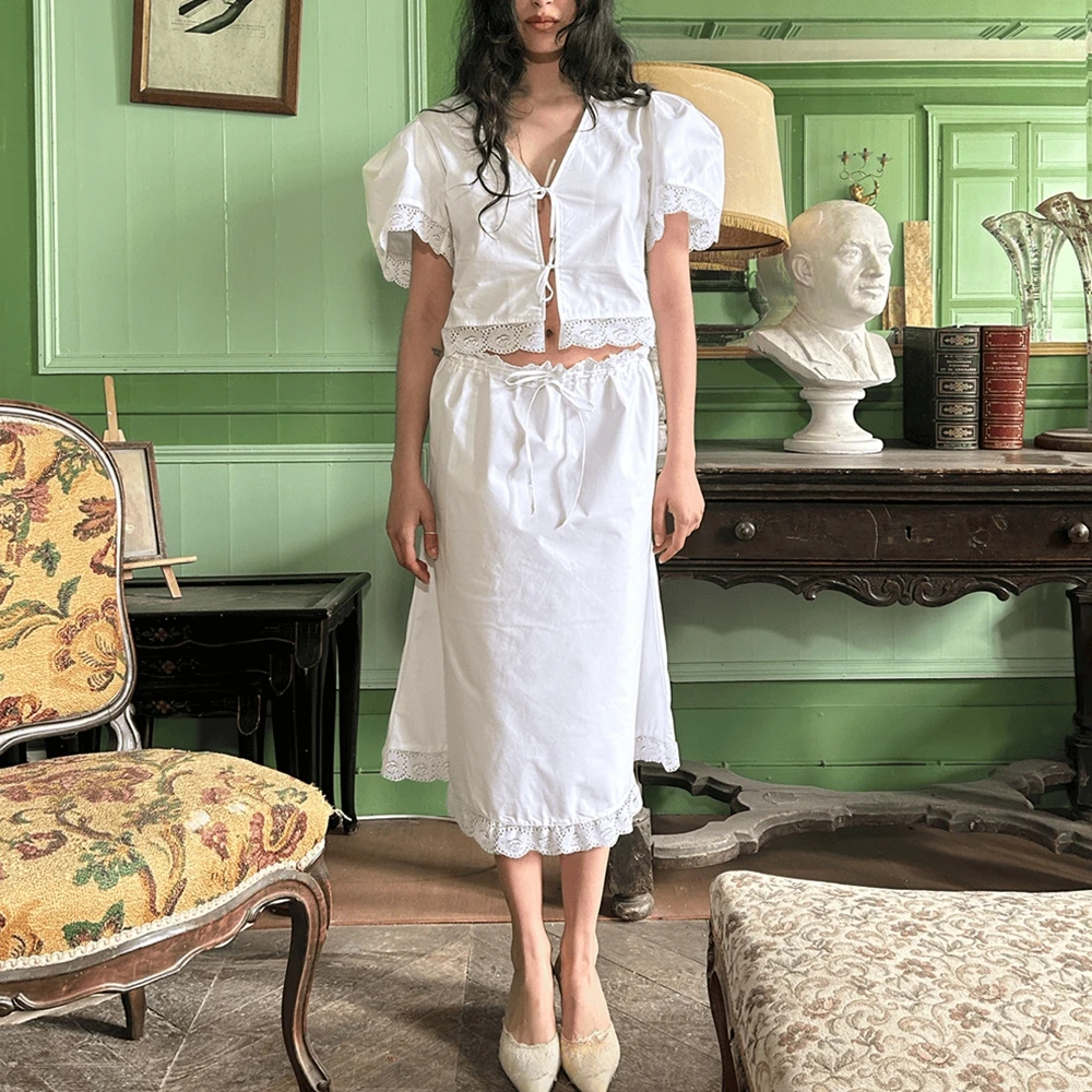 

Комплект из двух предметов: кружевная рубашка с коротким рукавом и бантом спереди и юбка миди