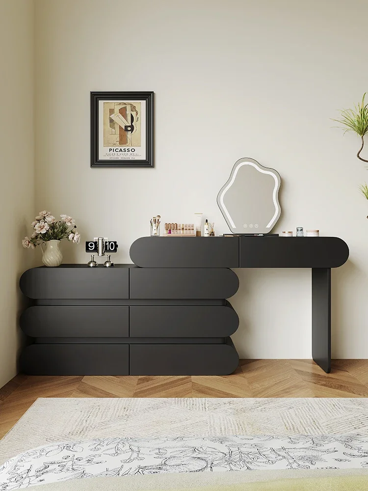 The bedroom is modern and simple, with a makeup table, cream style, black corner dresser and chest of drawers.