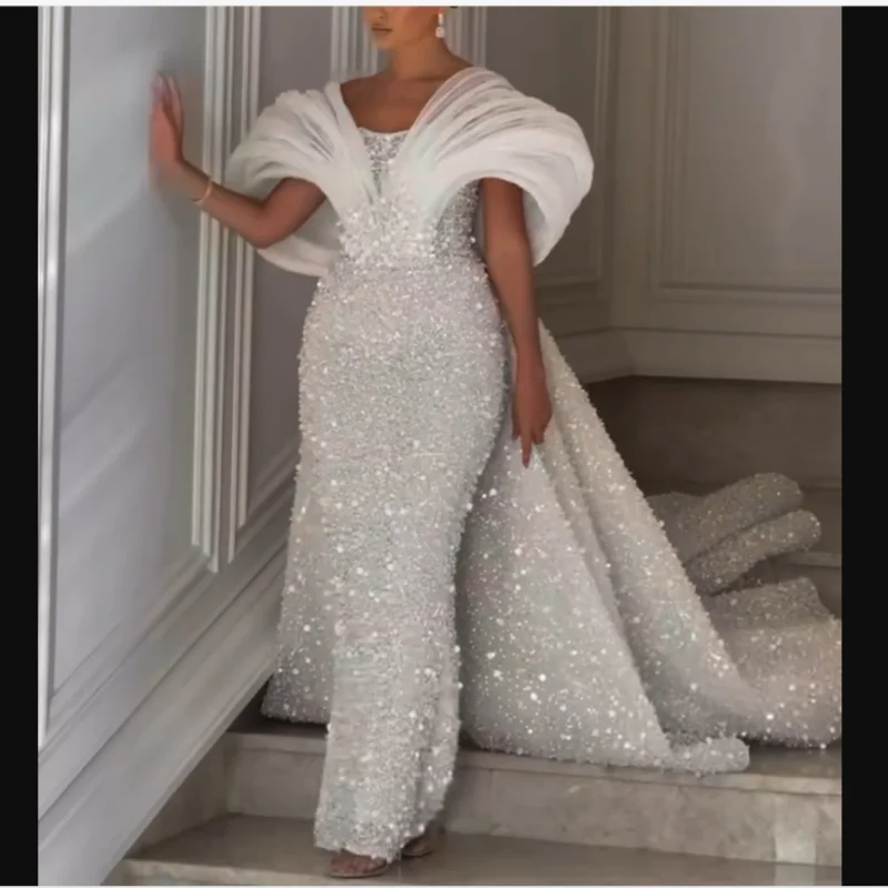 Suknia ślubna syrena z odkrytymi ramionami, zdobiona błyszczącymi, ciężkimi perłami i cekinami, z odpinanym trenem, luksusowa suknia ślubna.