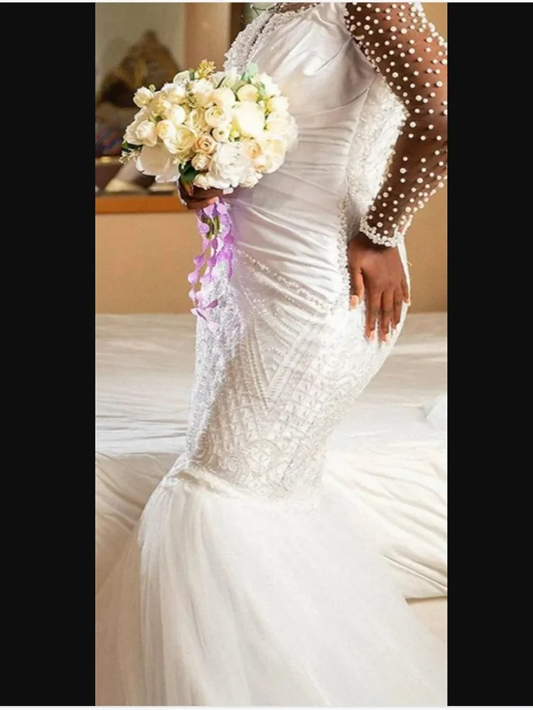 ชุดแต่งงานแบบแอฟริกันสั่งตัดพิเศษ คอเสื้อโปร่งประดับมุกเงางาม พร้อมชายกระโปรงยาวแบบสปีว์เทรน แขนยาวคลาสสิก หรูหรา