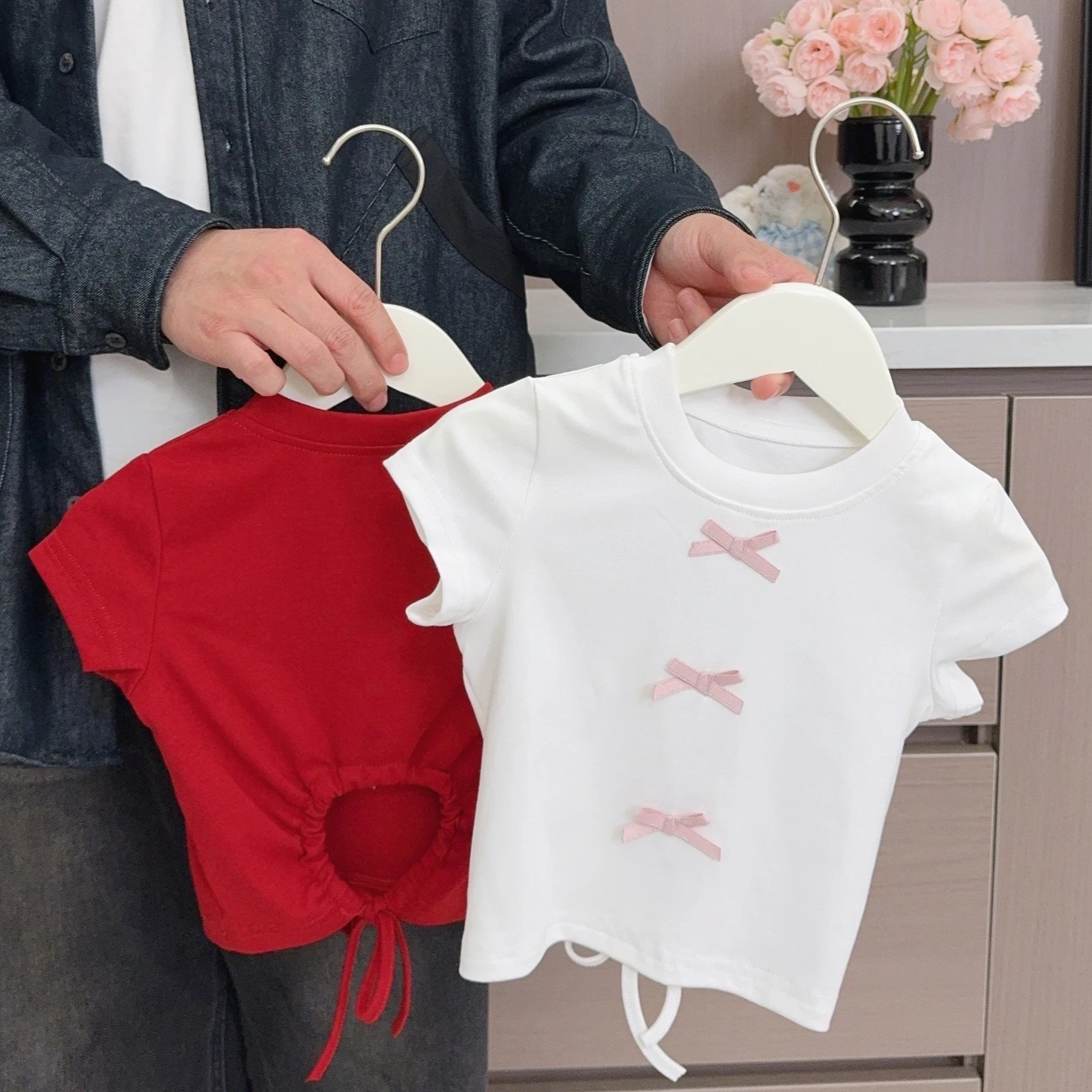 Camiseta Infantil Feminina 2026 Primavera e Verão Nova Coleção Roupa Infantil Estilo Coreano Menina Bebê Adorável Camiseta com Laço Vazado nas Costas