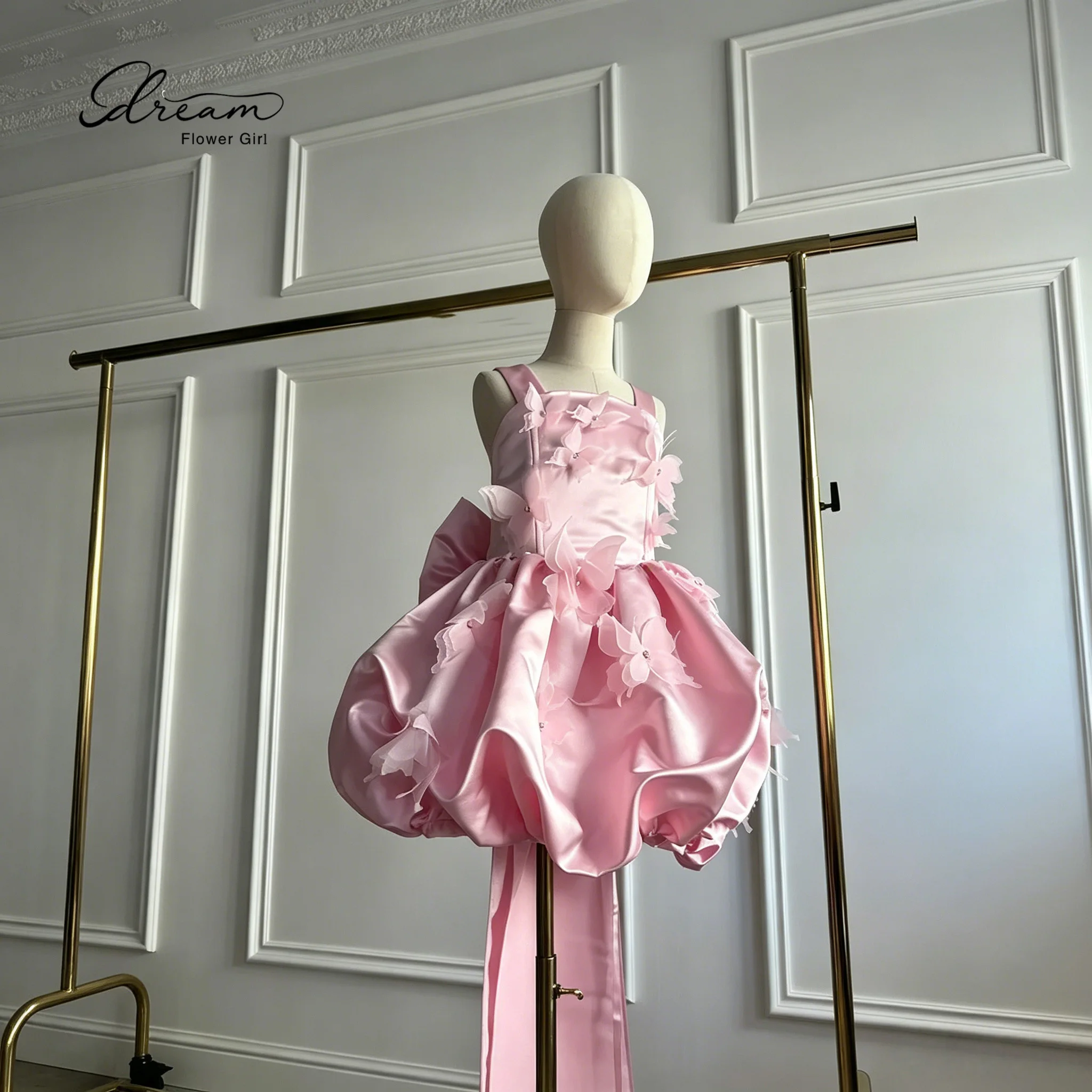 Adorable flower girl's pink satin knee-length evening dress, adorned with butterfly decorations and a bow design at the back.