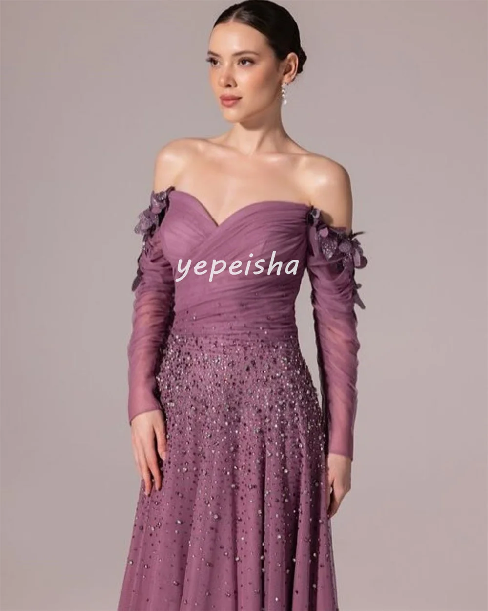 ชุดราตรีทรงเอไลน์แบบเปิดไหล่ ประดับด้วยผ้าทูลล์ระยิบระยับ แต่งดอกไม้ ลูกปัด และเลื่อม ดีไซน์หรูหรา