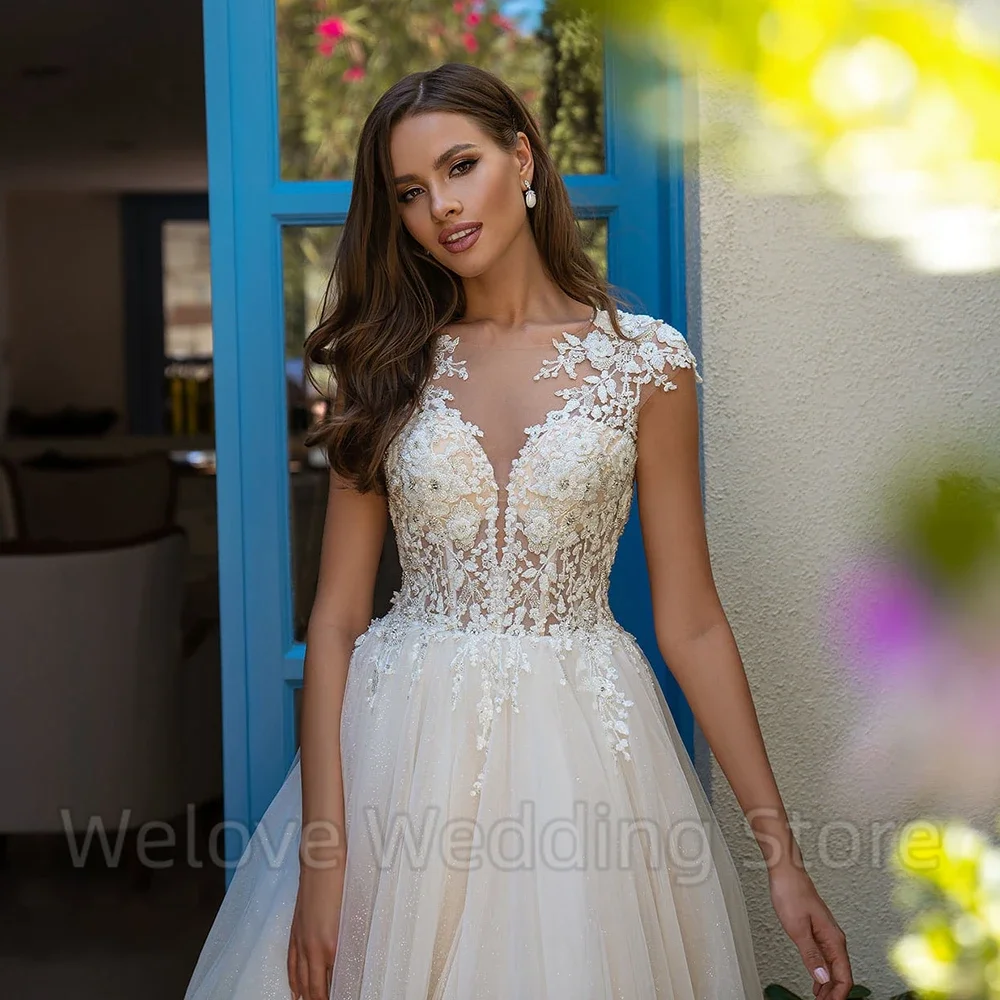 Nowoczesna suknia ślubna z tiulowymi aplikacjami, krótkimi rękawkami, iluzorycznym tyłem z guzikami, trenem typu sweep, długa do podłogi, formalna suknia ślubna.